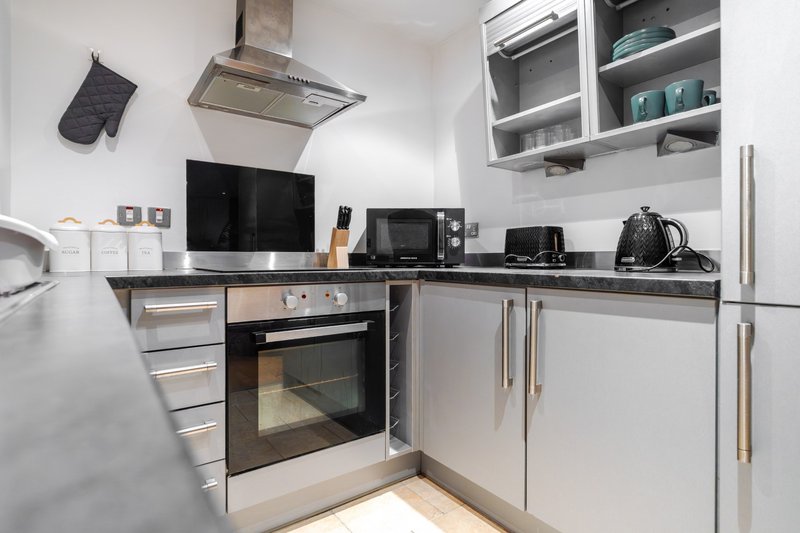 Modern white kitchen with stainless steel appliances, built-in oven, and wall-mounted shelving