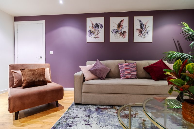 Living room with purple walls, beige sofa, brown armchair, framed bird artwork, potted plants