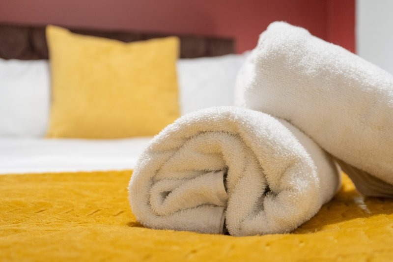 Bedroom with rolled towels on bed, yellow pillow and bedding, burgundy headboard