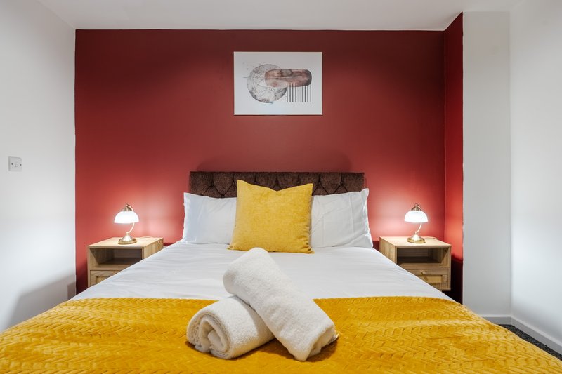 Modern bedroom with red accent wall, double bed, yellow bedding, and bedside lamps