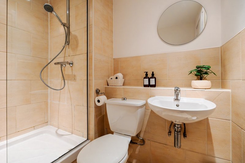 Modern bathroom with shower enclosure, toilet, round sink, mirror and shelving with toiletries