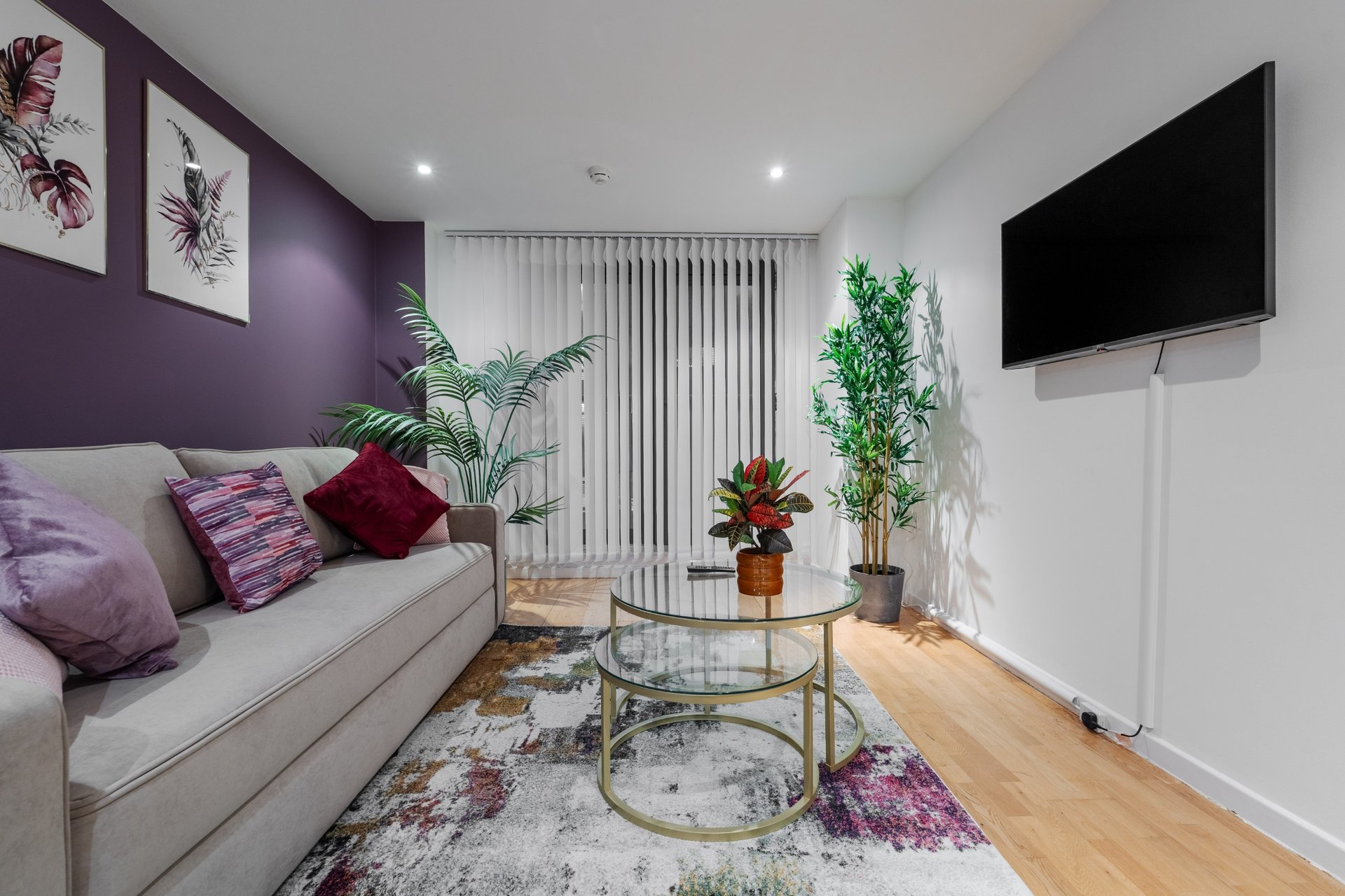 Modern living room with purple accent wall, cream sofa, decorative plants and wall-mounted TV