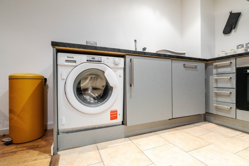 Utility room with integrated washing machine, grey cabinetry, and yellow waste bin