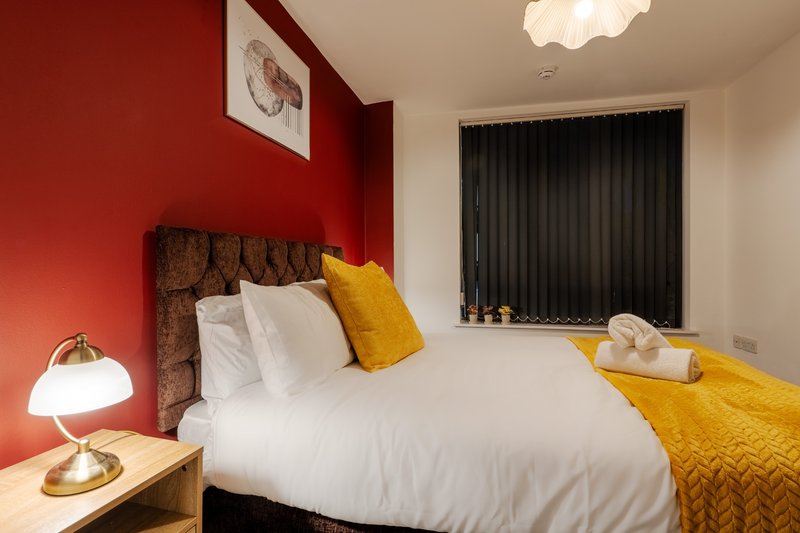Bedroom with double bed, red accent wall, yellow cushion and throw, bedside lamp