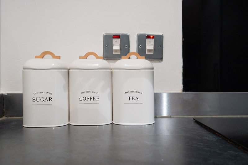 Kitchen countertop with three white ceramic storage jars labeled sugar, coffee and tea