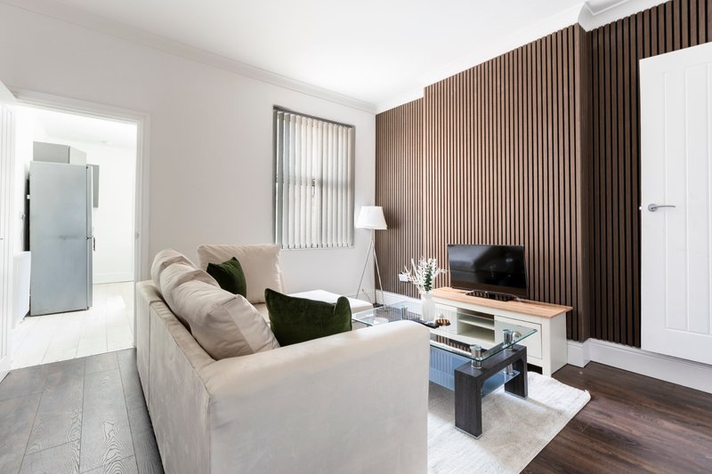 Modern living room with cream sofa, dark cushions, TV unit, brown curtains and wooden flooring