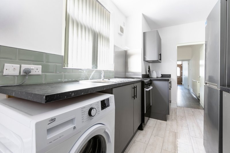Modern kitchen with washing machine, black countertops, grey cabinets and white tiled floor