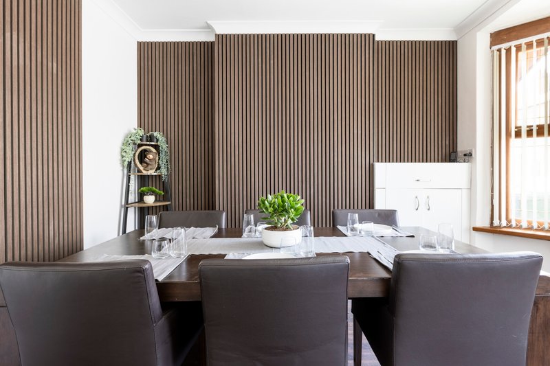 Modern dining room with dark table, upholstered chairs, vertical wood paneling, and indoor plants