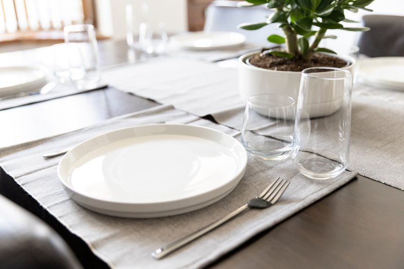 Dining table setting with white plate, glasses, cutlery and potted plant