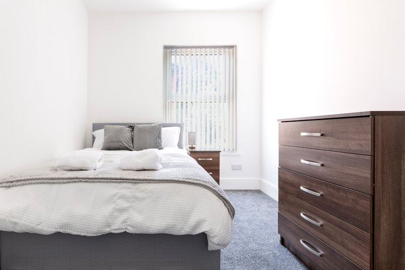 Bright bedroom with double bed, wooden chest of drawers, vertical blinds and grey carpet
