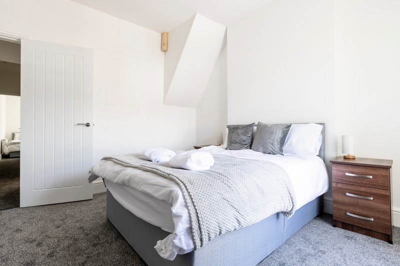 Bright bedroom with double bed, grey carpet, wooden bedside table and white wardrobe