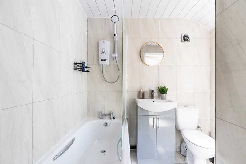 Modern bathroom with white tile, bathtub, shower, vanity sink, toilet and round mirror