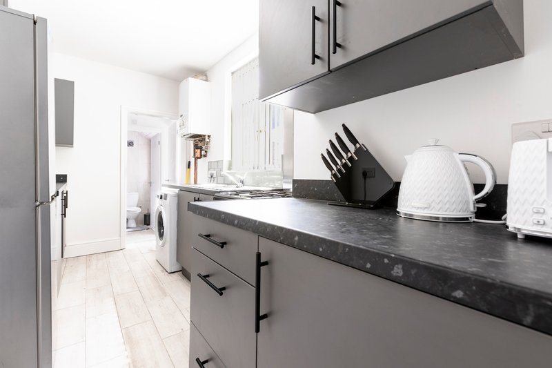Modern kitchen with grey cabinetry, black countertop, stainless steel appliances and white kettle