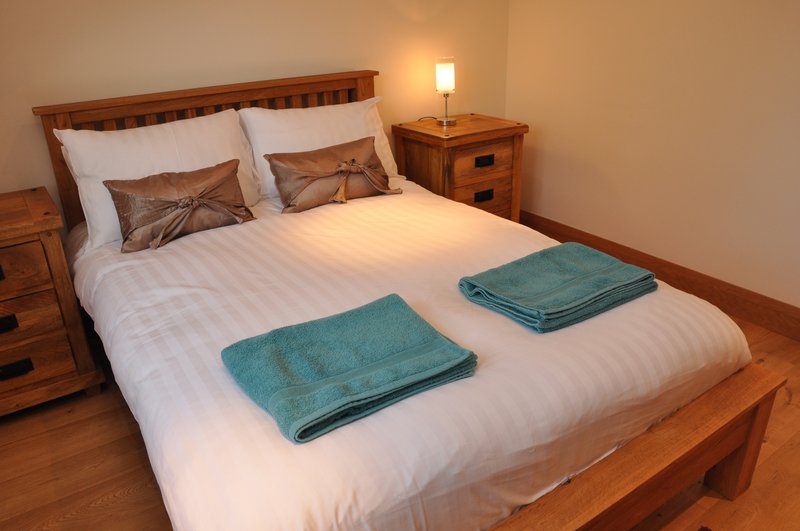 Wooden bed with white bedding, teal towels, brown cushions, and wooden bedside table with lamp