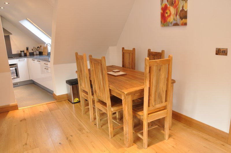 Open-plan kitchen and dining area with wooden table, chairs, and cream cabinetry