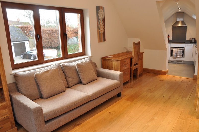 Open-plan living area with beige sofa, wooden dining table, hardwood flooring and kitchen