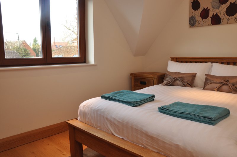 Bedroom with double bed, wooden frame, white bedding, teal towels, and windows with autumn trees visible