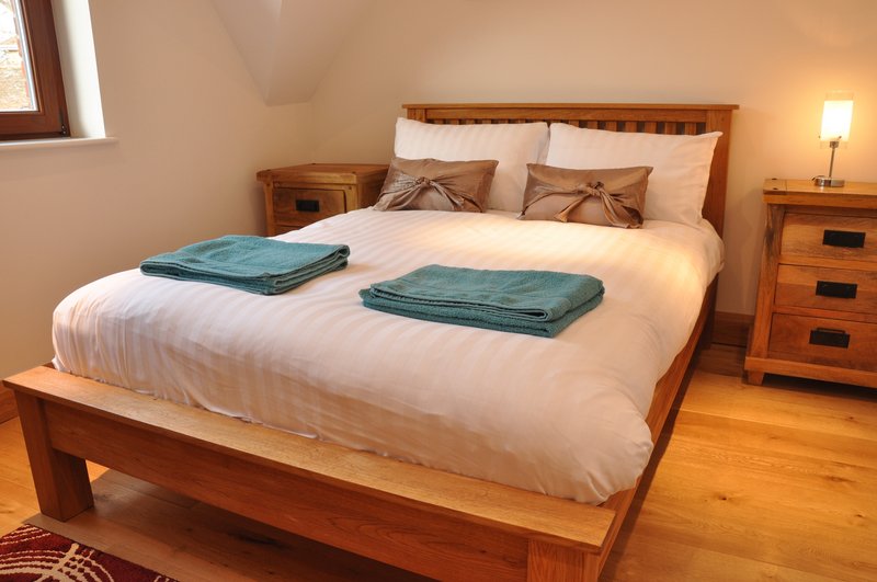 Bedroom with wooden bed, white bedding, teal towels, wooden furniture and warm lighting