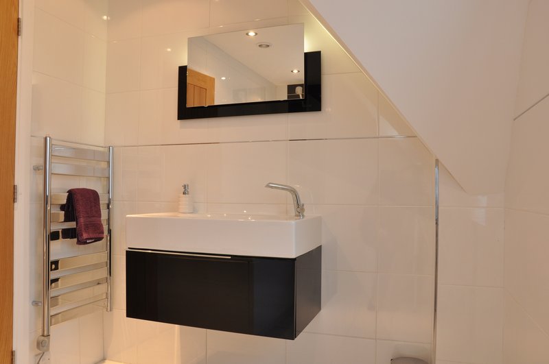 Modern bathroom with wall-mounted black vanity, white sink, heated towel rail and mirror