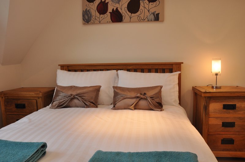 Bedroom with double bed, wooden headboard, bedside tables, lamp and wall art