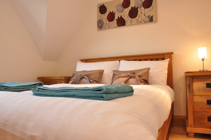 Bedroom with wooden bed frame, white bedding, decorative pillows and folded towel