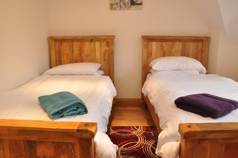 Twin bedroom with wooden bed frames, white bedding, folded blankets and patterned rug