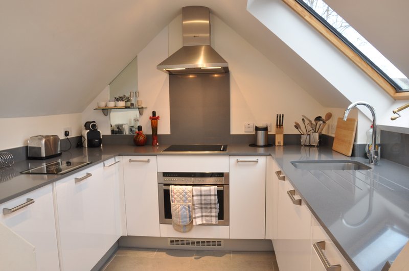 Modern attic kitchen with white cabinetry, stainless steel appliances, and sloped ceiling