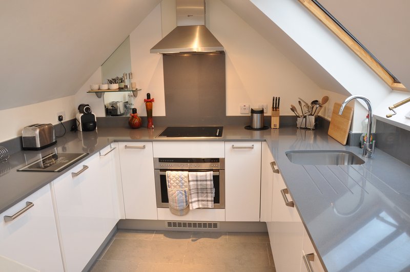 Modern attic kitchen with white cabinetry, dark countertop, integrated appliances and skylight