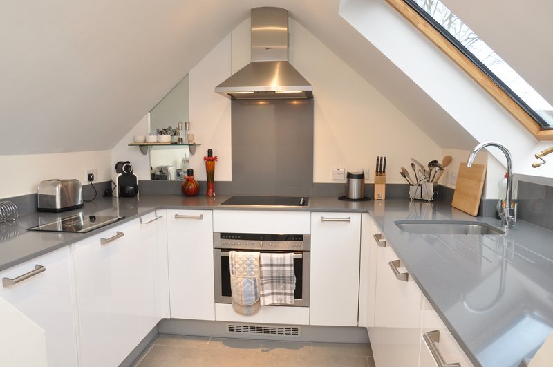 Modern attic kitchen with white cabinetry, stainless steel appliances, and skylight window