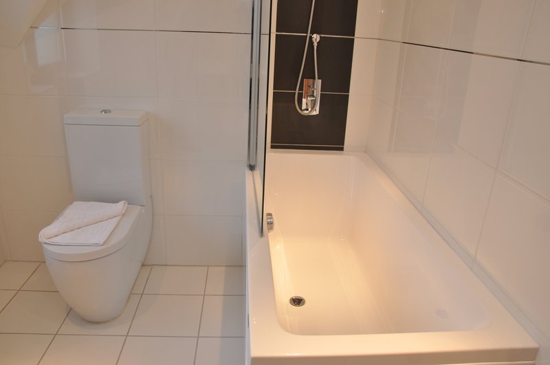 Modern bathroom with white toilet, bathtub, shower enclosure and neutral tile walls