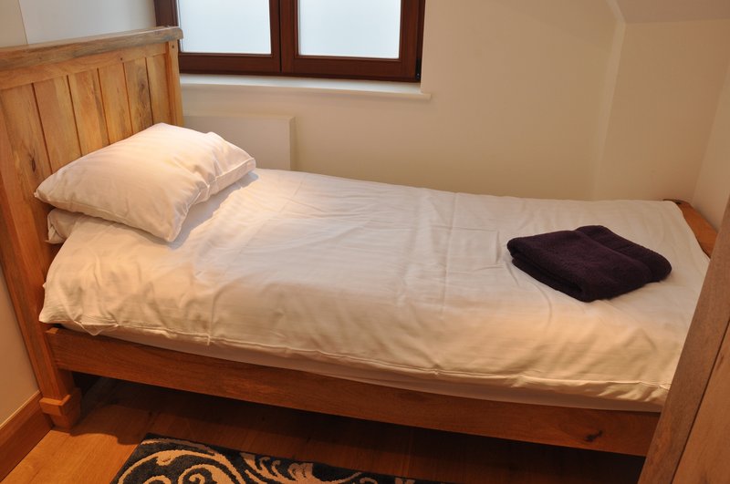 Single wooden bed with white bedding, pillow, and dark towel on mattress