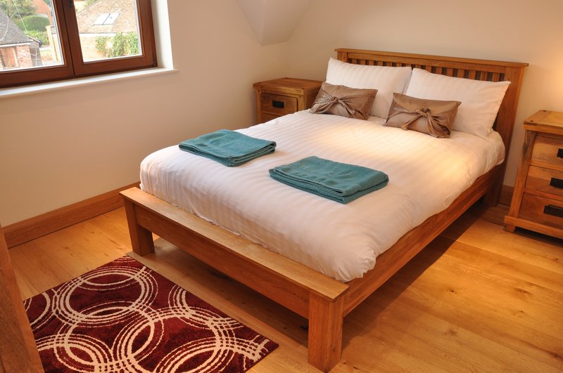 Wooden-framed double bed with white bedding and teal throws, wooden nightstands, patterned rug, and window