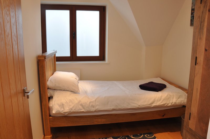 Small bedroom with wooden single bed, white bedding, pillow and dark cushion