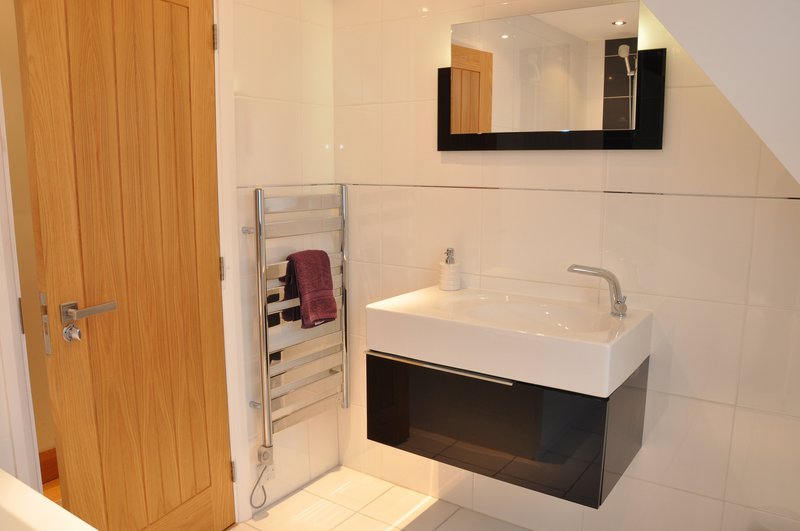 Modern bathroom with white sink, heated towel rail, mirror and wooden door