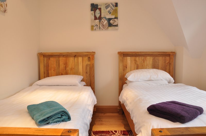 Bedroom with two single beds, wooden headboards, white bedding and folded throws