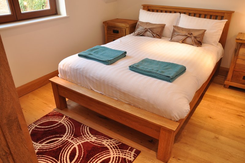 Wooden bed with white bedding, teal towels, and burgundy patterned rug in bright bedroom