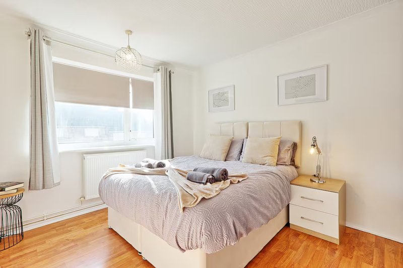 Bright modern bedroom with double bed, wooden floor, bedside table and window with curtains