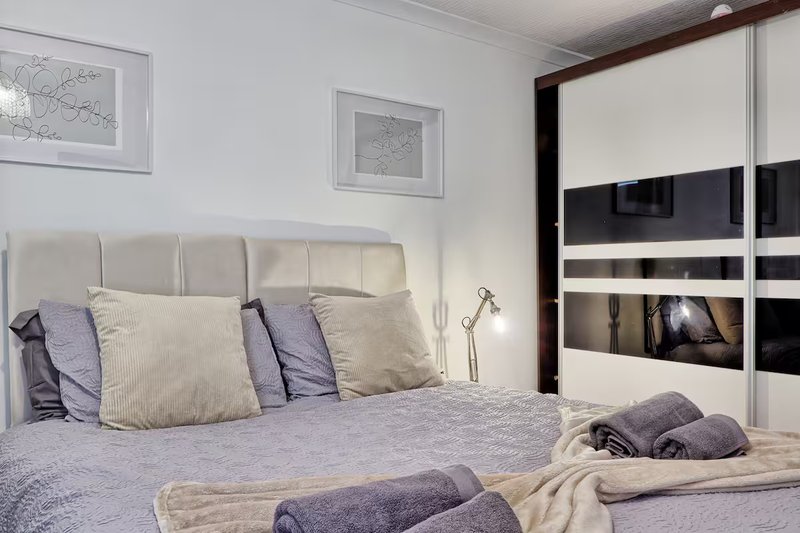 Modern bedroom with grey upholstered headboard, double bed, mirrored wardrobe and framed wall art