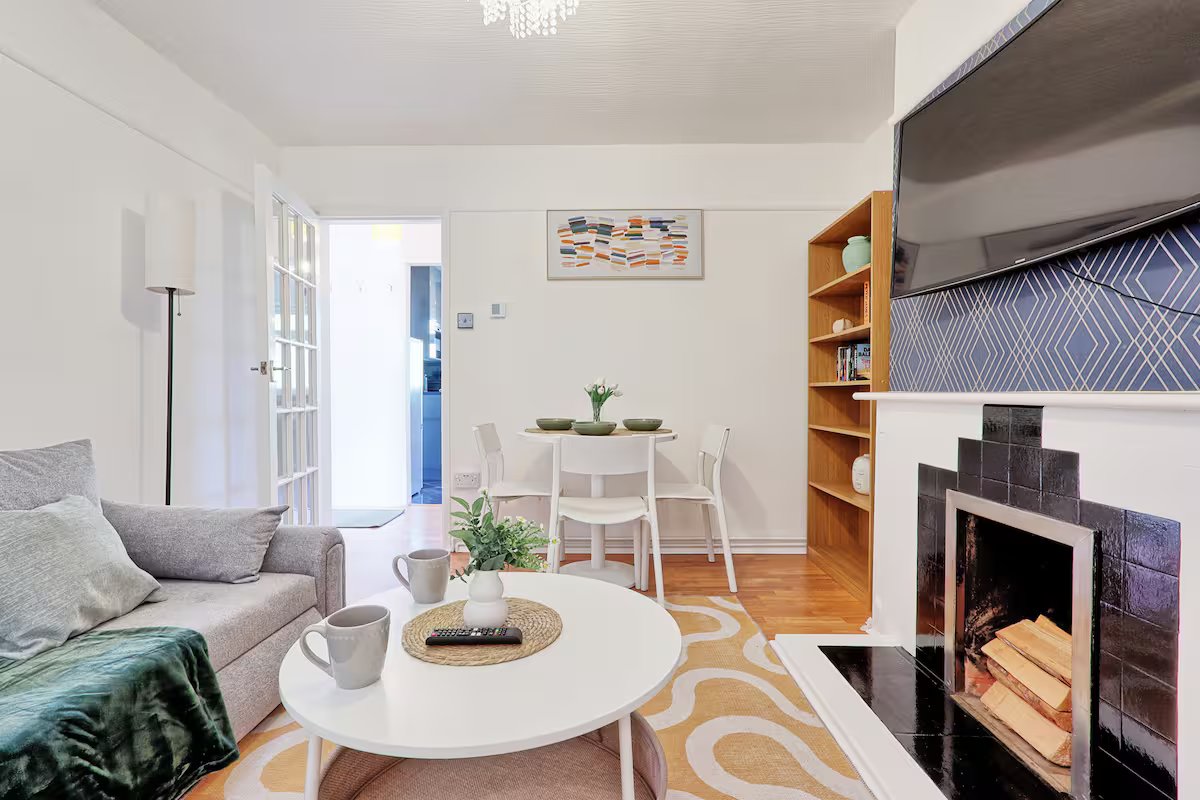 Bright open-plan living room with sofa, round coffee table, fireplace and wooden shelving unit