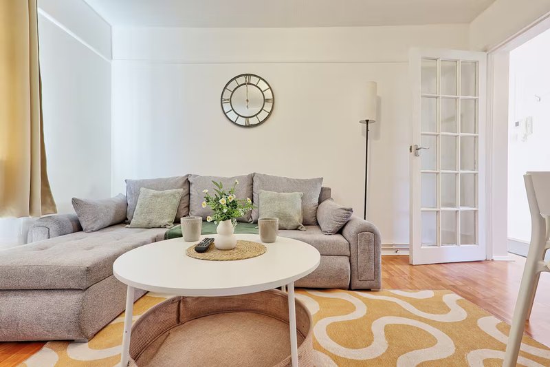 Living room with gray sectional sofa, white round coffee table, wall clock and patterned rug