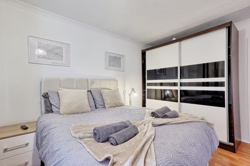 Modern bedroom with double bed, blue bedding, rolled towels, and black mirrored wardrobe
