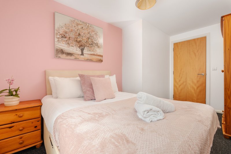 Pink bedroom with double bed, wooden nightstand, framed tree artwork, and wooden doors