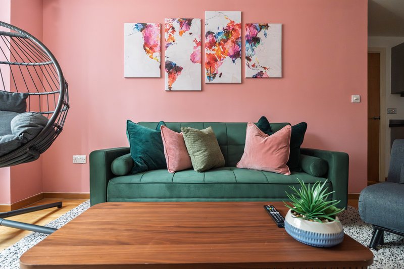 Modern living room with green sofa, pink walls, wooden table and world map artwork