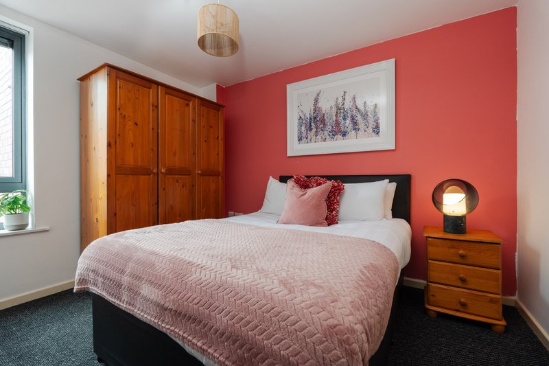 Bedroom with double bed, red accent wall, wooden wardrobe and bedside table