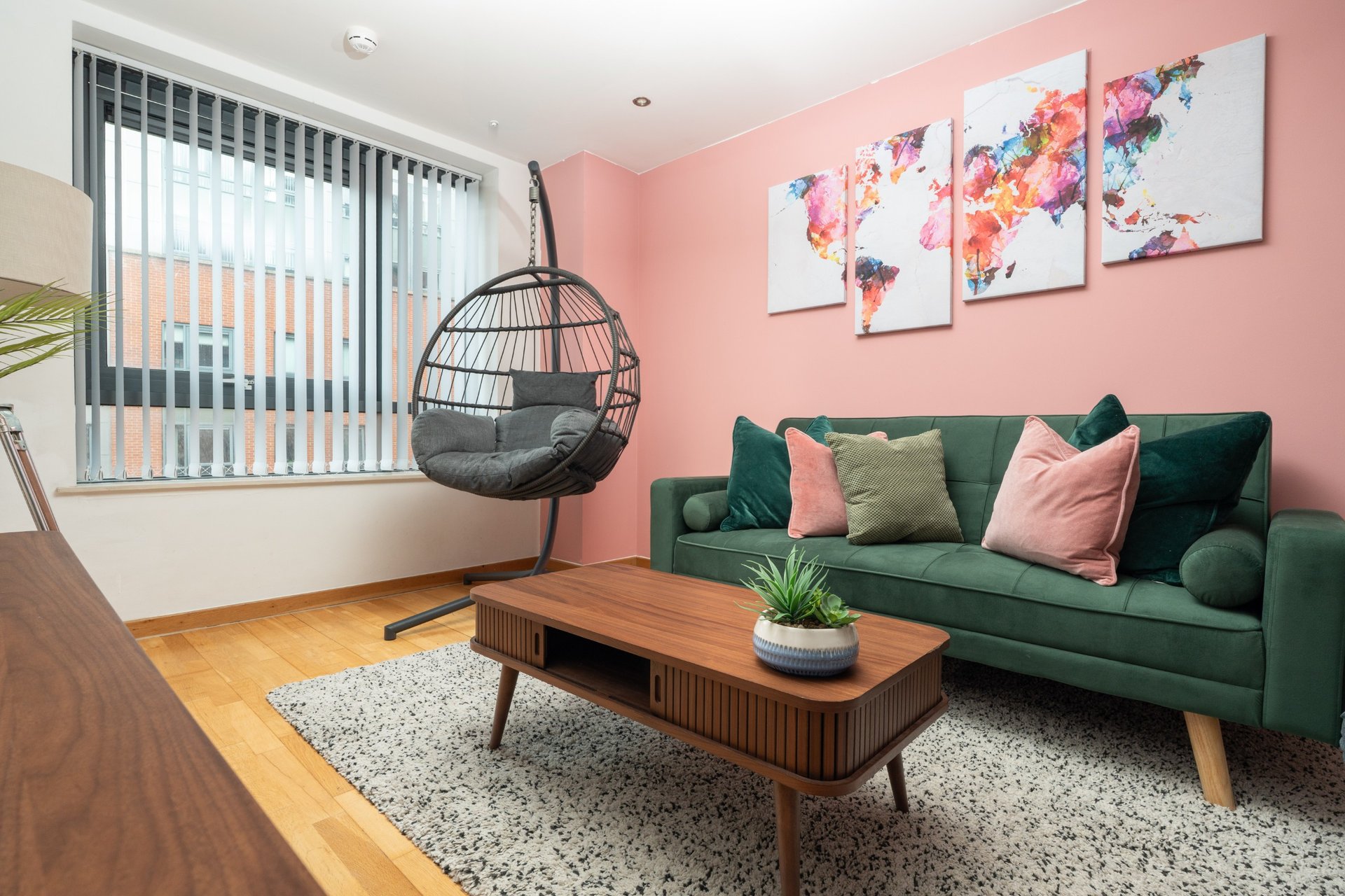 Modern living room with pink walls, green sofa, wooden coffee table and hanging chair