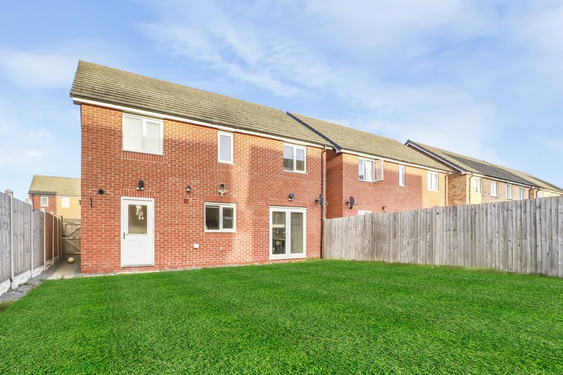 Rear exterior of modern brick house with green lawn and wooden fence