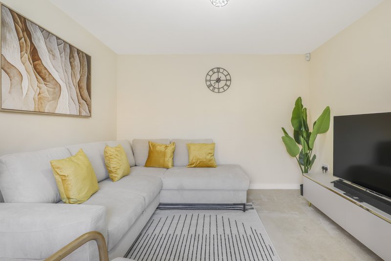 Bright living room with grey corner sofa, yellow cushions, wall art, and television