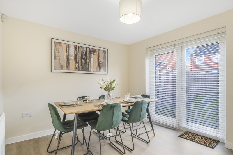 Dining area with wooden table, green chairs, framed wall art and glass doors