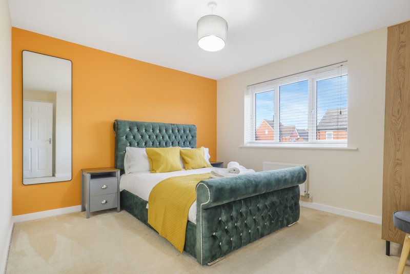 Modern bedroom with teal upholstered bed, yellow bedding, orange accent wall and large window