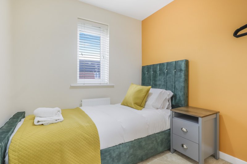 Bright bedroom with single bed, green headboard, yellow accent wall and bedside table